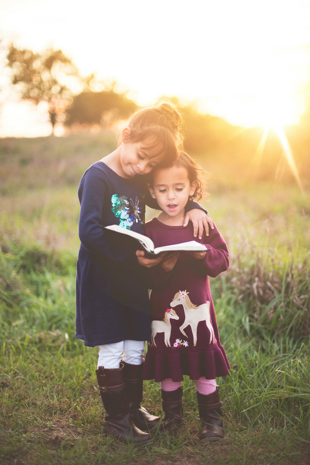 Girls and book by Bible Verse Daily girl's left hand wrap around toddler while reading book during golden hour