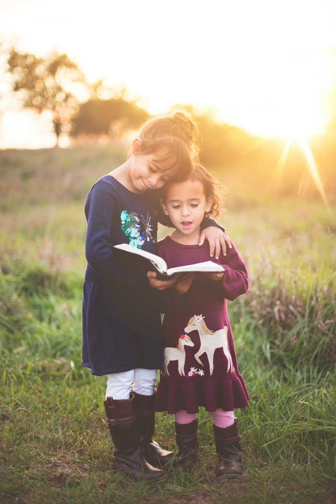 Girls and book by Bible Verse Daily girl's left hand wrap around toddler while reading book during golden hour