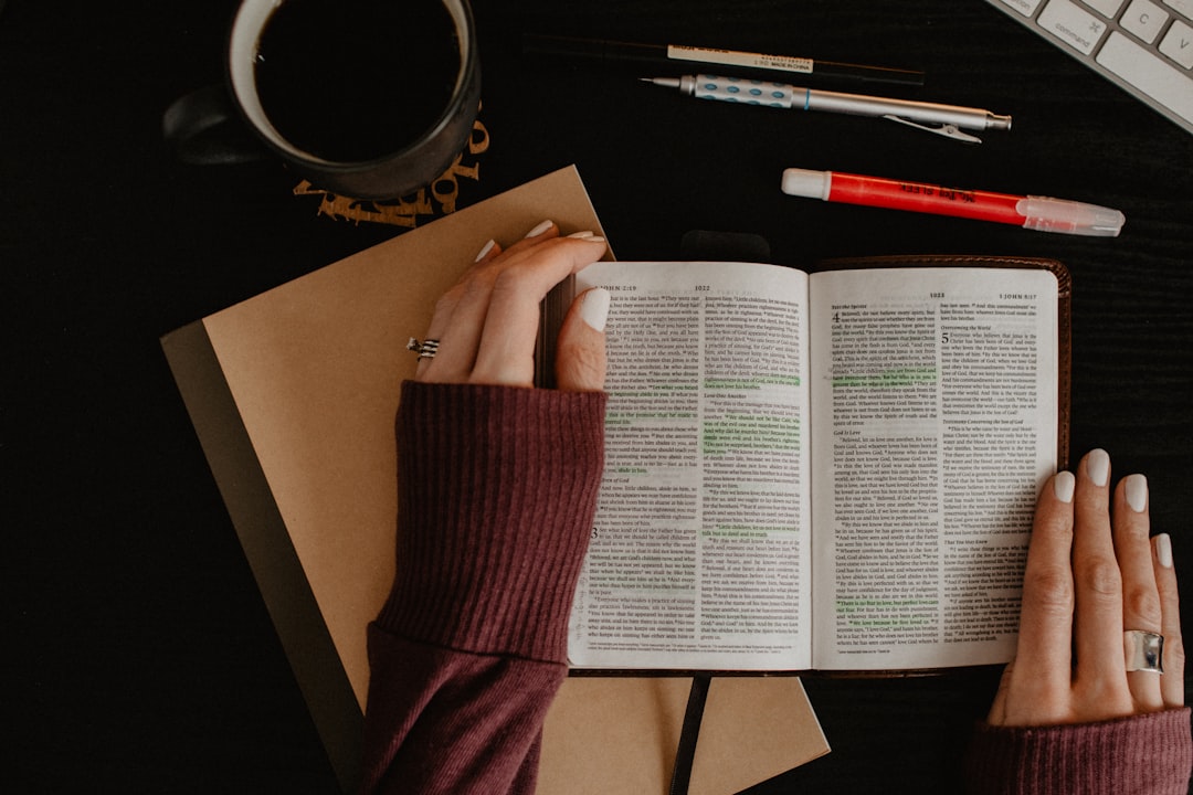 Woman's hands with open Bible by Bible Verse Daily person in maroon long sleeve shirt holding white printer paper