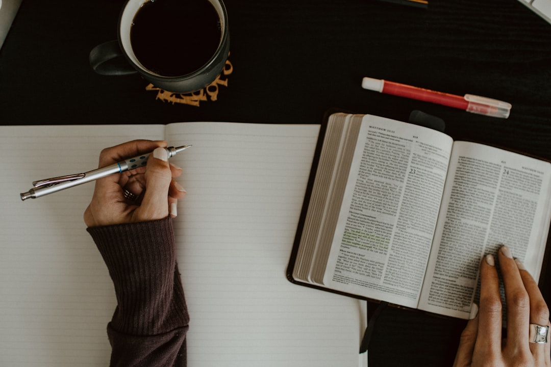 Woman's hands with Bible open and blank notebook by Bible Verse Daily person writing on white paper